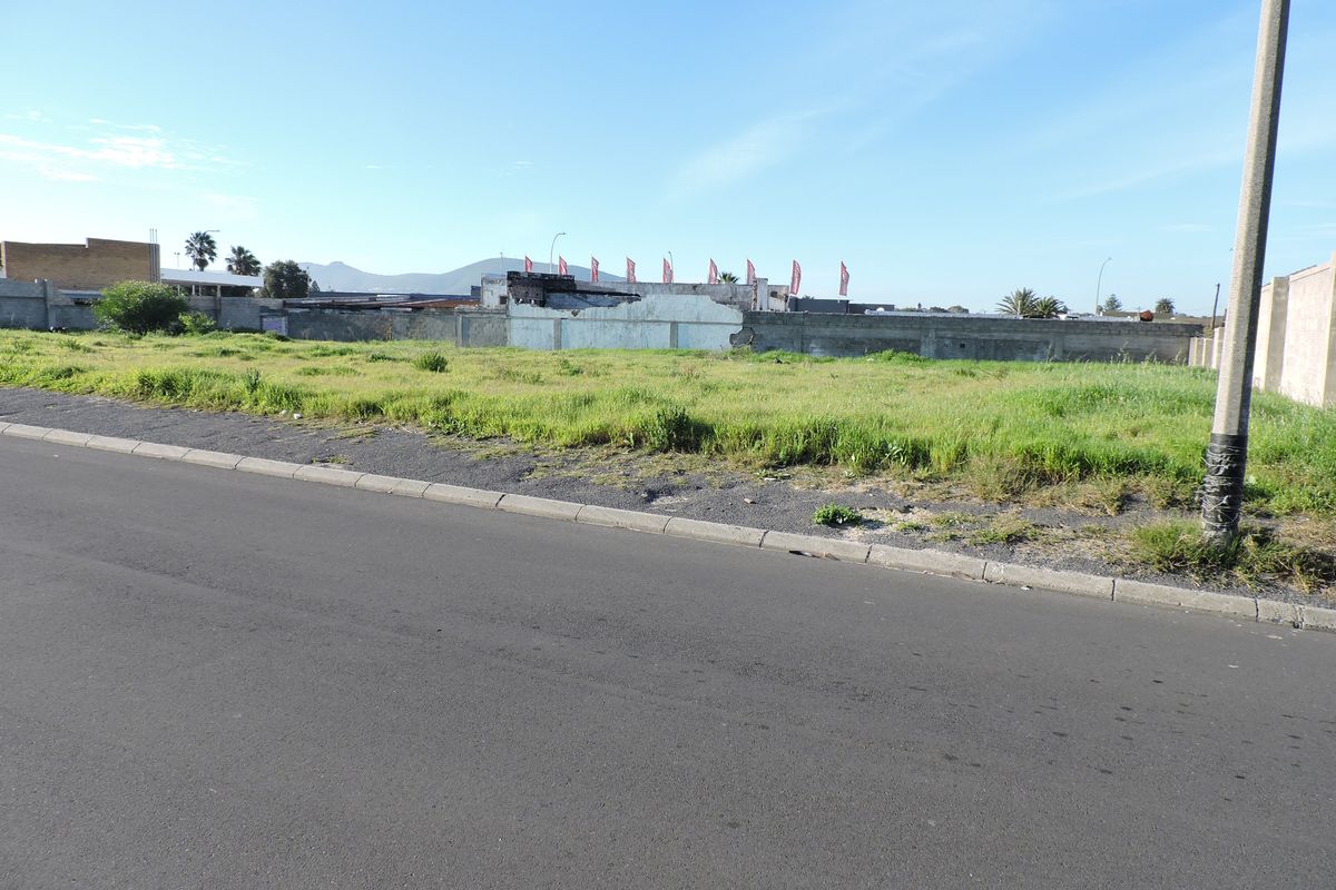 A vacant residential plot featuring a grassed surface, bordered by a perimeter wall and accessible via a paved street.