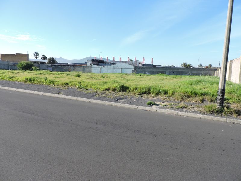 A vacant residential plot featuring a grassed surface, bordered by a perimeter wall and accessible via a paved street.
