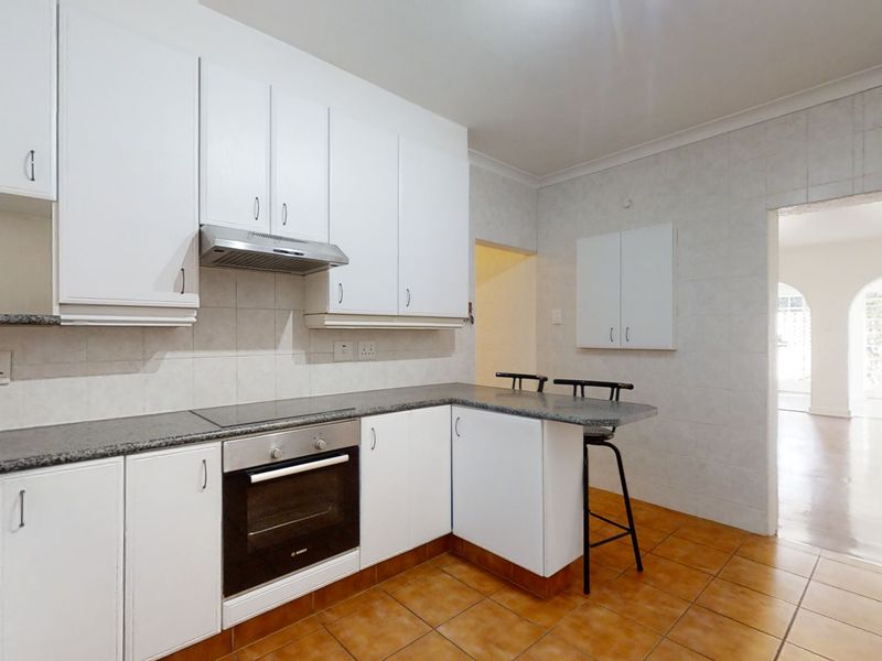 Functional kitchen featuring white cabinetry, granite countertops, built-in oven, hob, and extractor fan with tiled flooring and splashbacks.