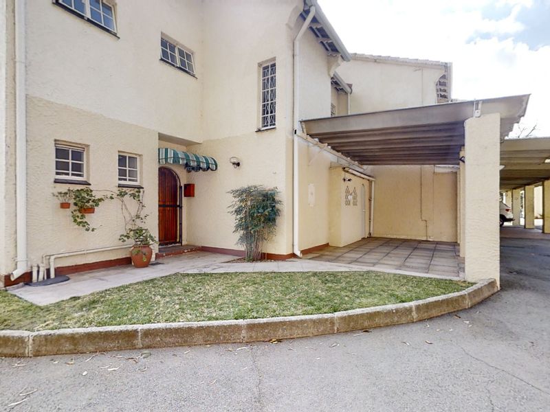 Front elevation of the townhouse featuring a paved carport, small garden area, and a secure entrance with a decorative awning.