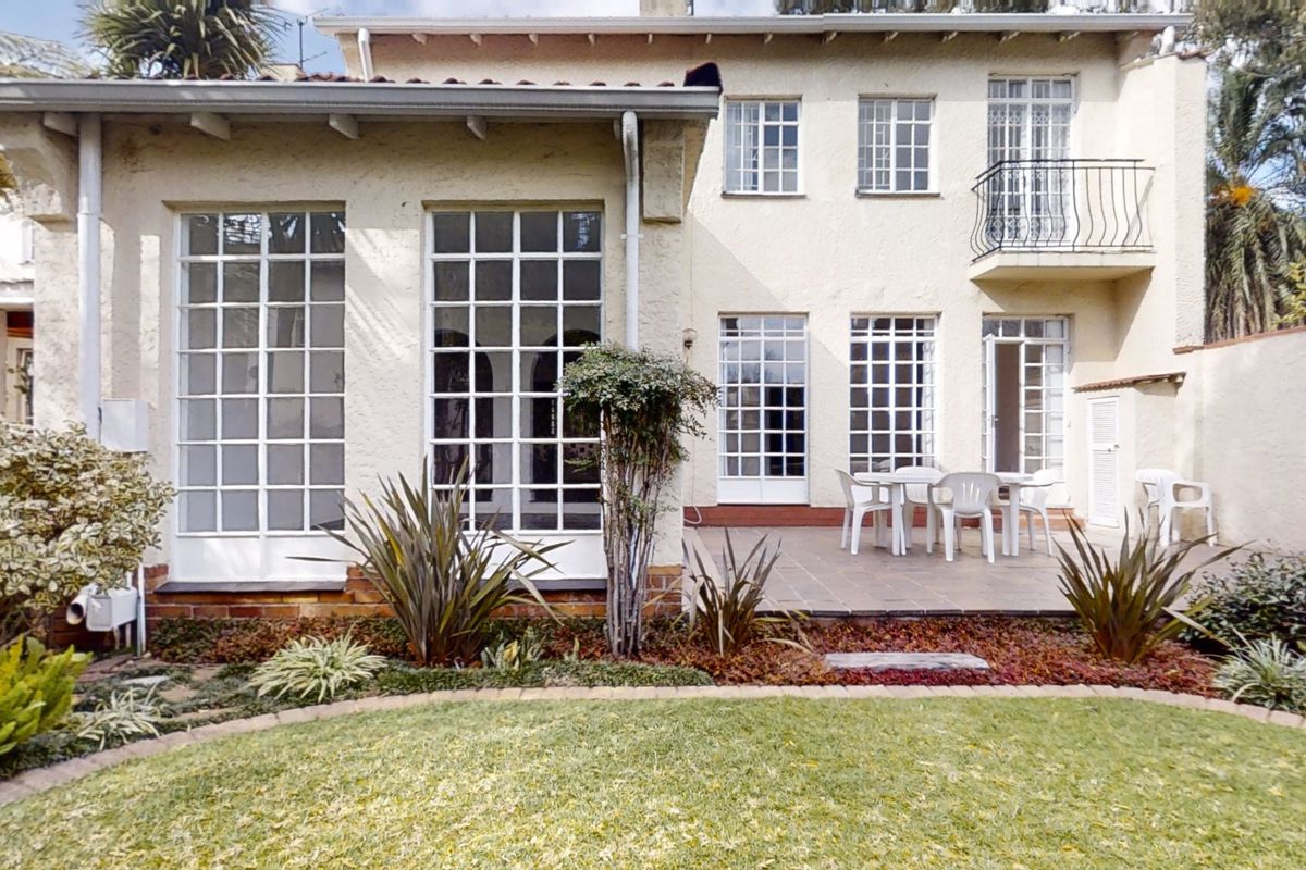Rear view of the townhouse featuring a tiled patio, multi-pane windows, french doors, and a small upper-level balcony with wrought iron railing.