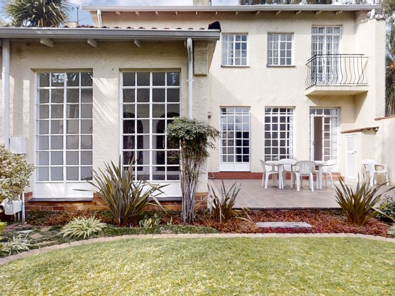 Rear view of the townhouse featuring a tiled patio, multi-pane windows, french doors, and a small upper-level balcony with wrought iron railing.