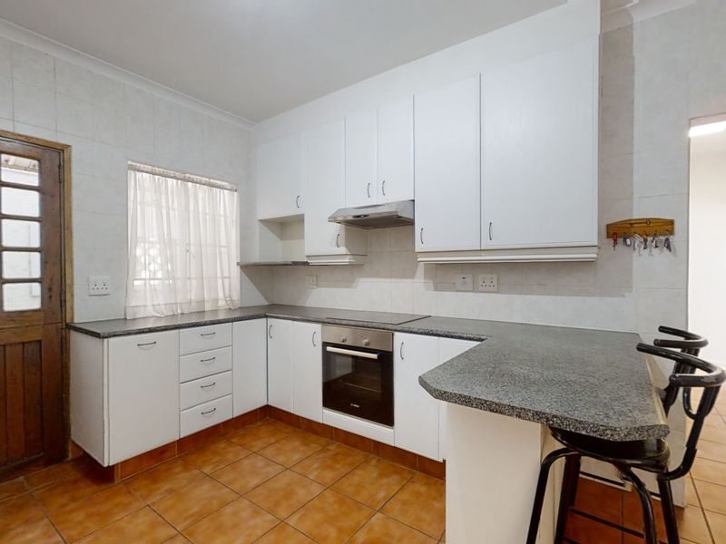 Functional kitchen featuring white cabinetry, granite-look laminate countertops, built-in oven and hob, tiled splashbacks, and terracotta-style floor tiles.