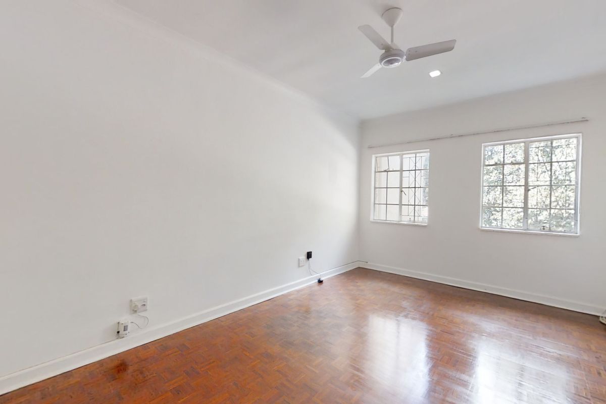 A bright, empty bedroom featuring polished parquet flooring, a ceiling fan, and windows fitted with security bars.