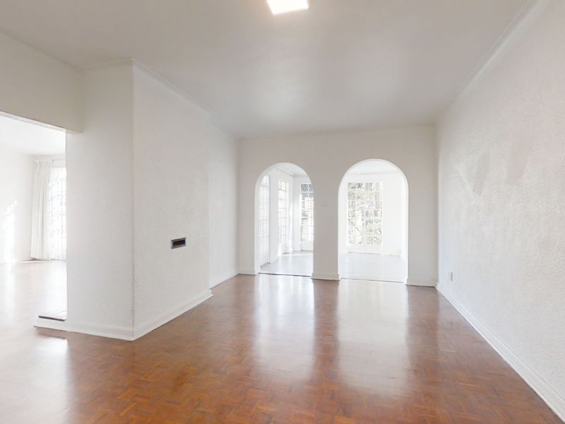 Spacious, empty living area featuring classic parquet flooring and elegant arched doorways leading to adjacent rooms with natural light.