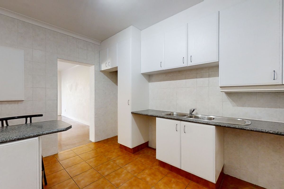 A functional kitchen featuring white built-in cabinetry, laminate countertops, a double stainless steel sink, and tiled flooring, offering a clean and neutral space.