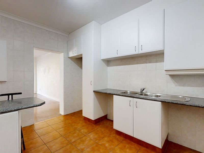 A functional kitchen featuring white built-in cabinetry, laminate countertops, a double stainless steel sink, and tiled flooring, offering a clean and neutral space.