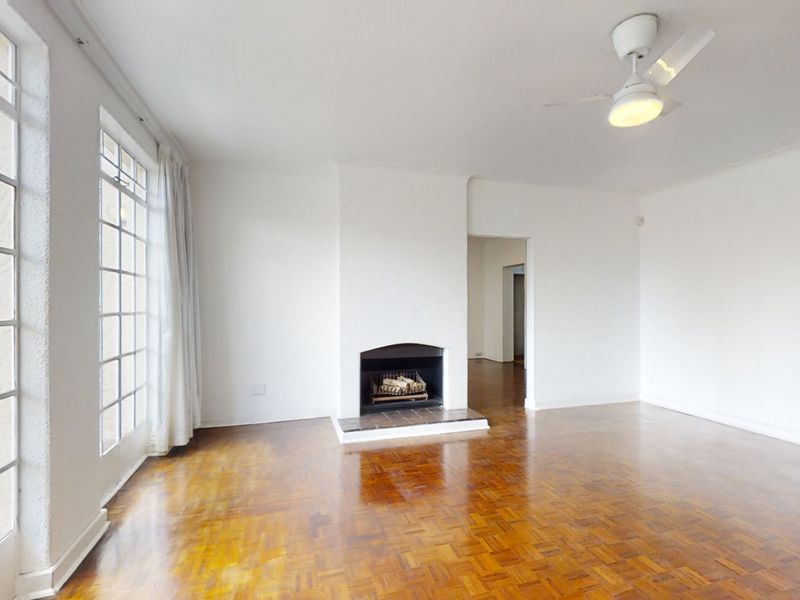 Spacious living room featuring classic parquet flooring, a central fireplace, and large french doors providing natural light and access to the exterior.
