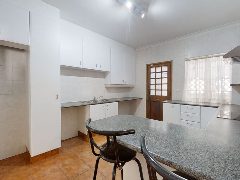 Functional kitchen featuring white cabinetry, granite countertops, tiled flooring, and an integrated extractor fan, offering a practical layout for daily meal preparation.