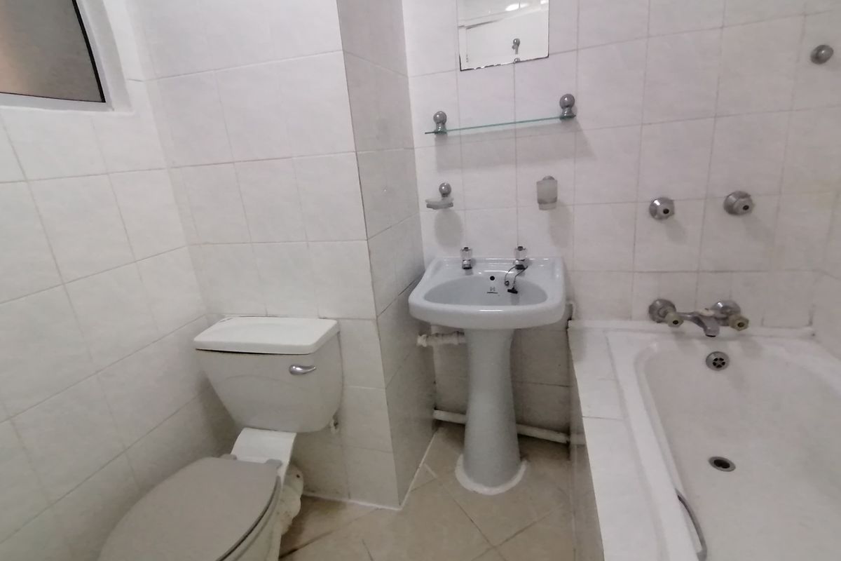 A functional bathroom featuring a pedestal basin, bathtub, and toilet with full-height wall tiling and tiled flooring.