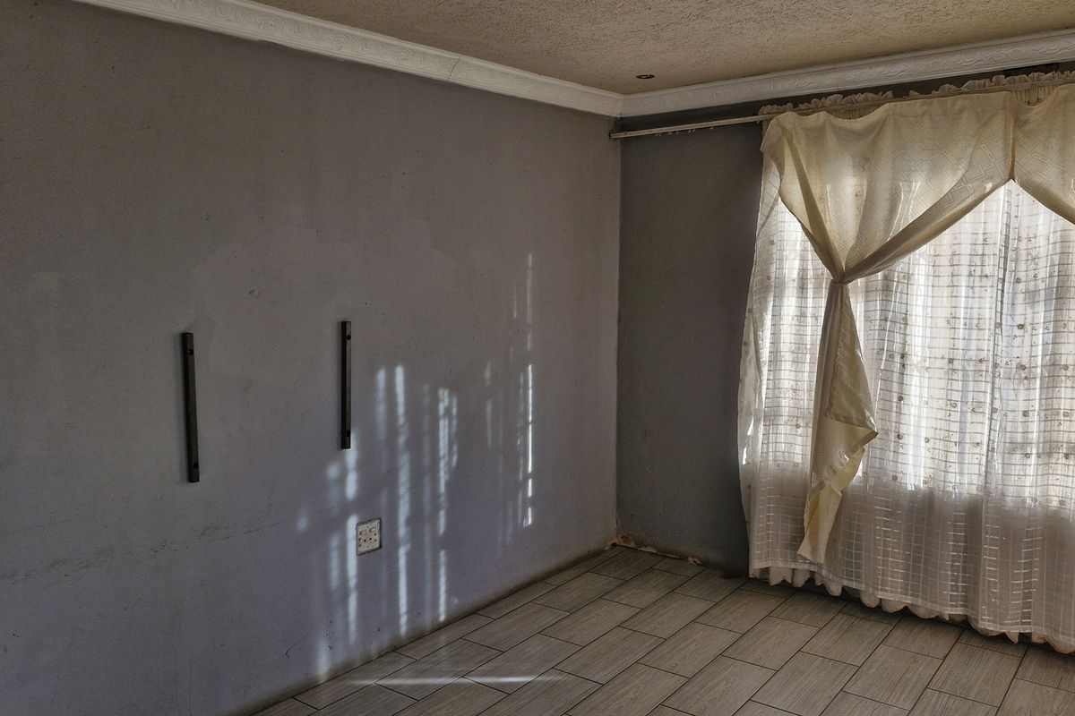 An empty living room featuring tiled flooring, ceiling cornices, and grey walls with visible surface imperfections, ready for renovation or staging.