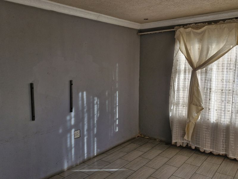 An empty living room featuring tiled flooring, ceiling cornices, and grey walls with visible surface imperfections, ready for renovation or staging.