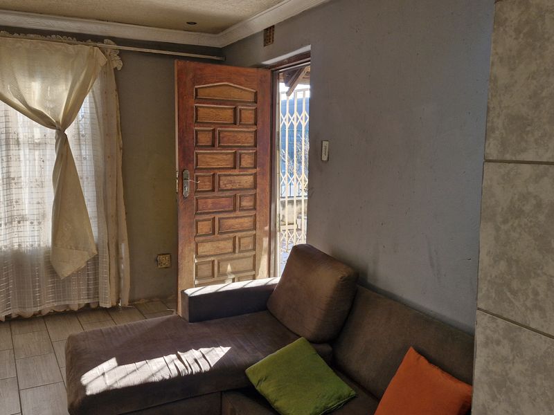 A living room area featuring tiled flooring, a timber panel door leading to an exterior space, and neutral wall finishes.