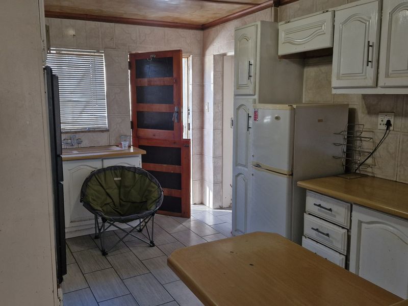 A functional kitchen featuring built-in cabinetry, tiled backsplash, and tiled flooring, providing a practical layout with direct access to an exterior door.