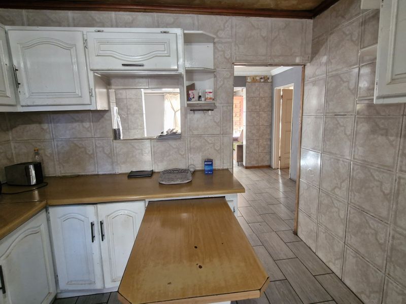 A dated kitchen featuring white cabinetry, laminate countertops with a pull-out breakfast bar, and full-height ceramic wall tiling leading into an adjacent living area.