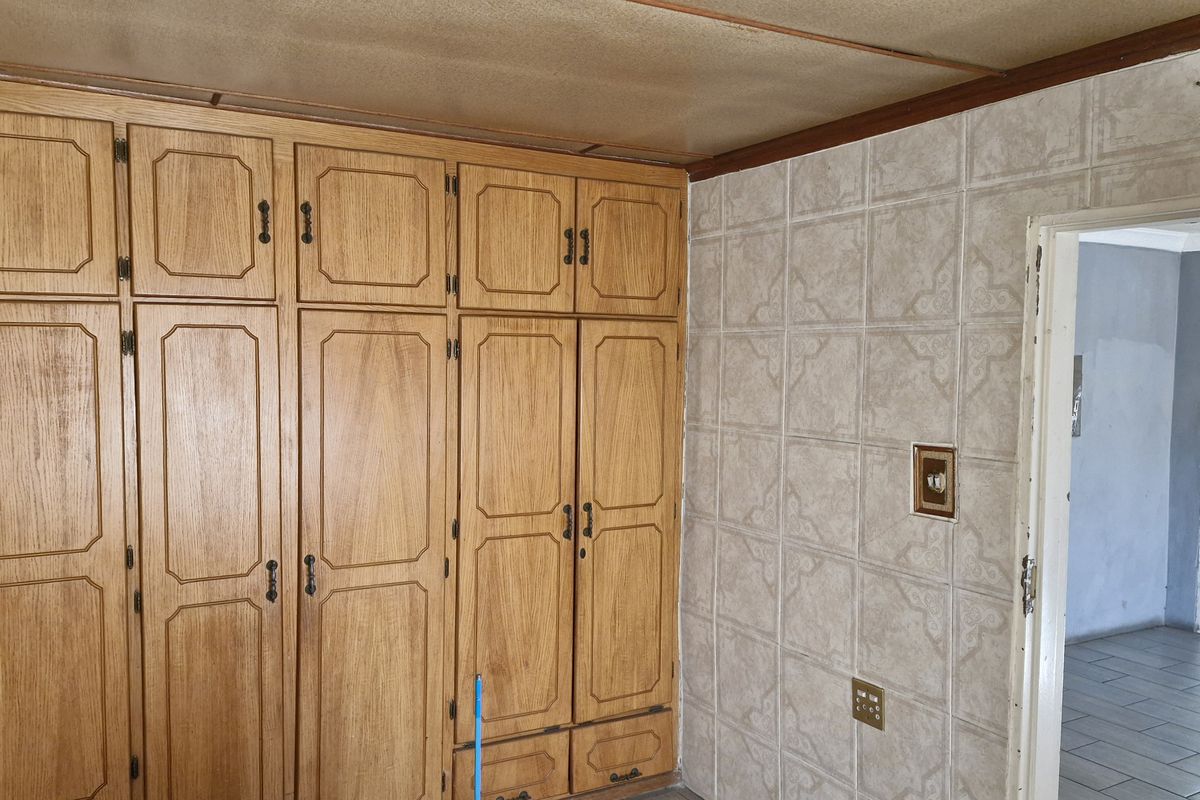 Bedroom featuring extensive built-in wooden cabinetry and tiled wall finishes, offering significant storage potential in a dated interior space.