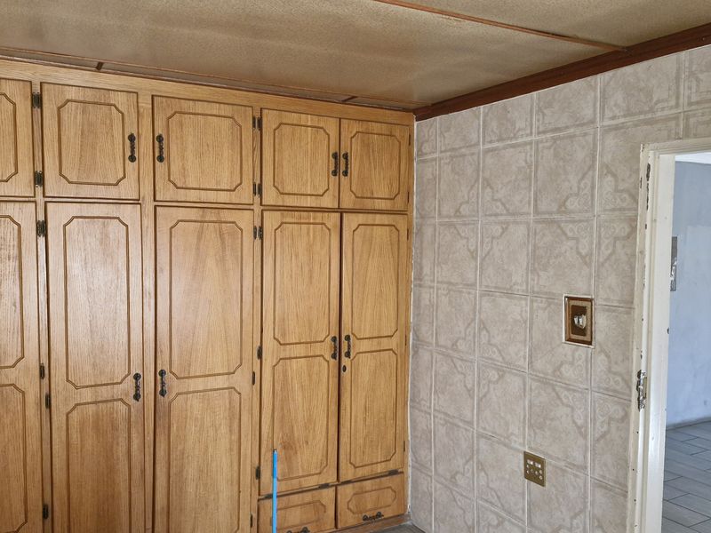 Bedroom featuring extensive built-in wooden cabinetry and tiled wall finishes, offering significant storage potential in a dated interior space.