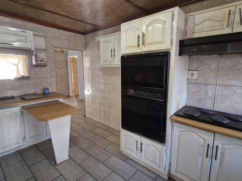 A dated kitchen featuring built-in cabinetry, tiled walls, and integrated appliances, offering a functional layout ready for modern renovation and cosmetic updates.