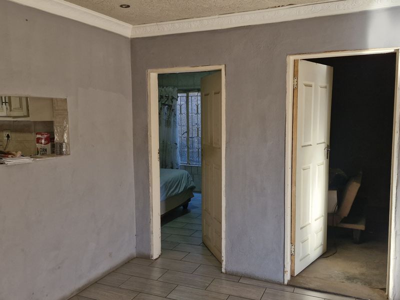An empty living area featuring tiled flooring, coving, and a serving hatch connecting to the kitchen, with doorways leading to adjacent rooms.