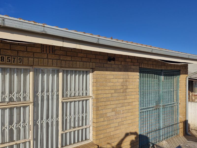 Front exterior view of a brick house featuring security gates and metal window frames, showing signs of weathering and maintenance requirements.