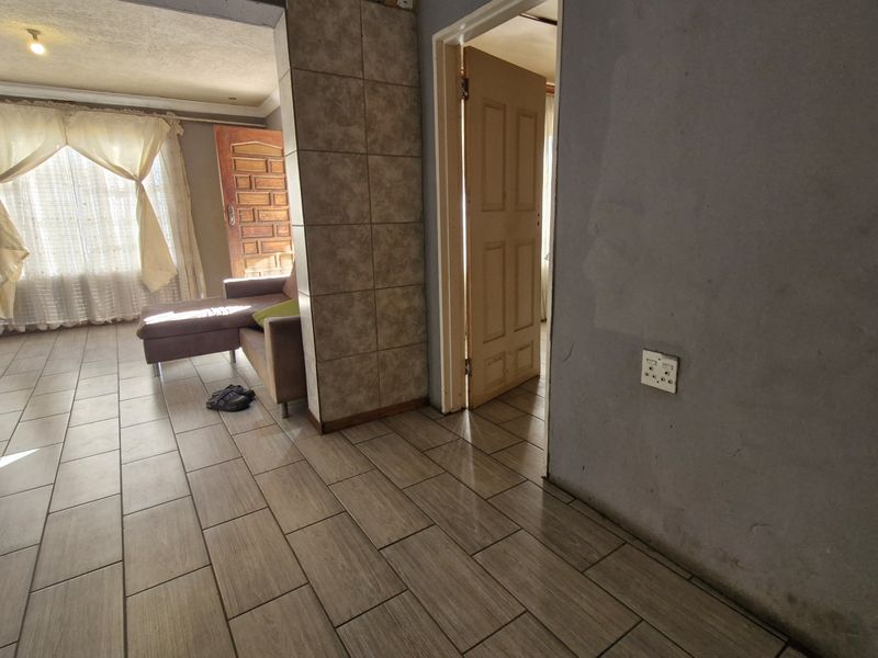A living area featuring tiled flooring and a tiled structural pillar, showing signs of wear on the walls and requiring cosmetic updates.