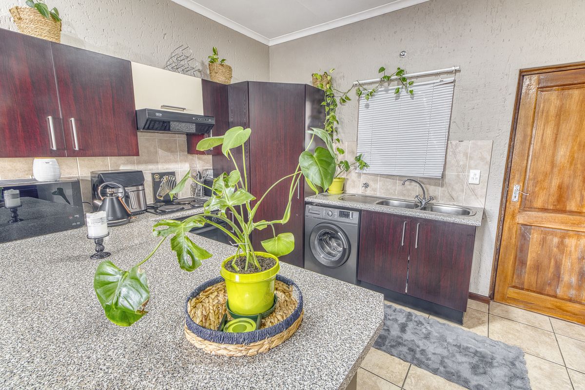 Functional kitchen featuring dark wood cabinetry, granite countertops, integrated washing machine, and built-in cooking appliances with tiled flooring.