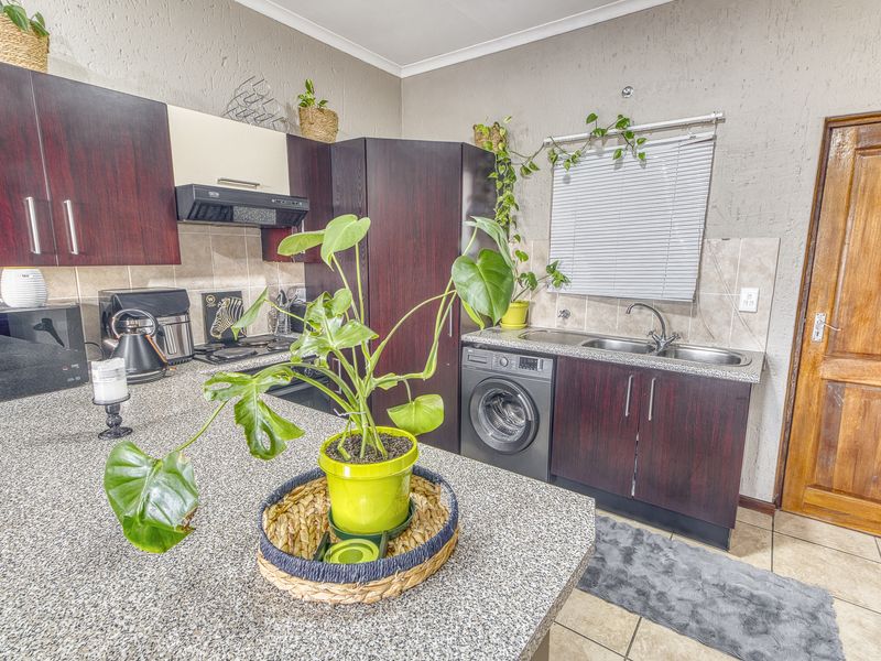 Functional kitchen featuring dark wood cabinetry, granite countertops, integrated washing machine, and built-in cooking appliances with tiled flooring.