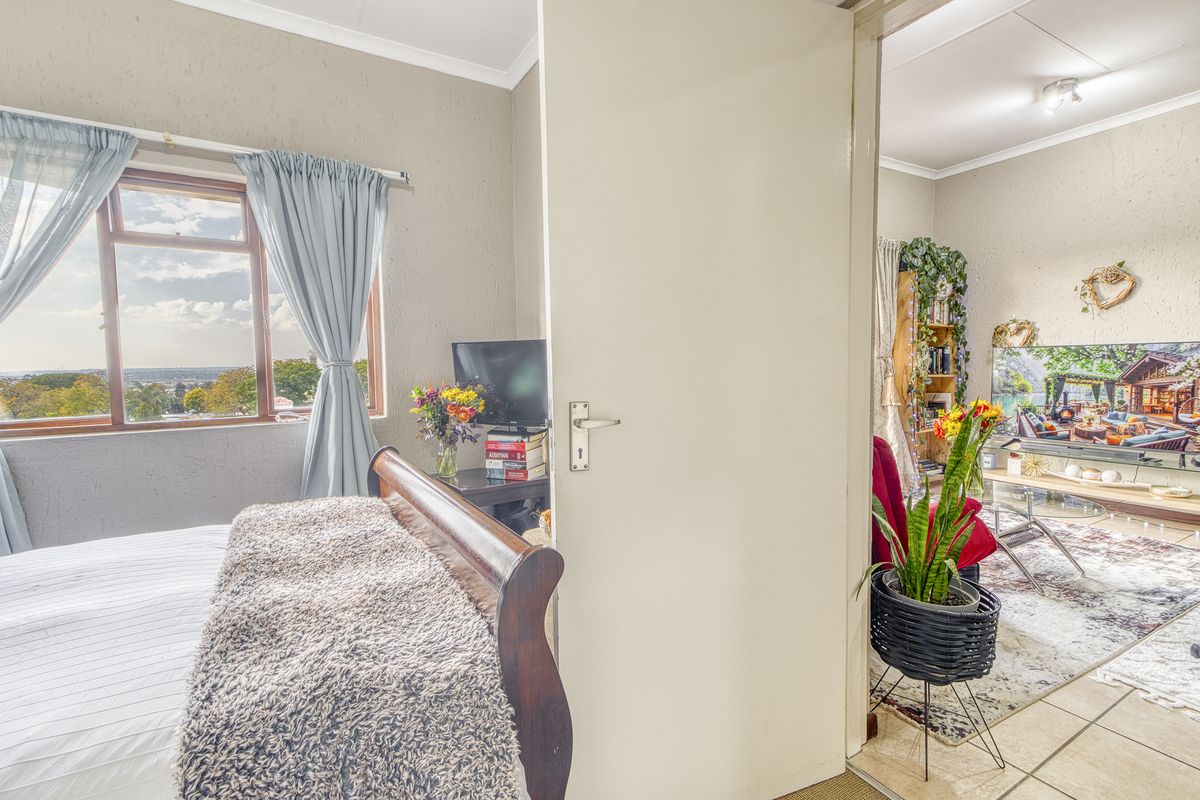 A bedroom featuring a window with exterior views, leading into an adjacent living area with tiled flooring and coved ceilings.