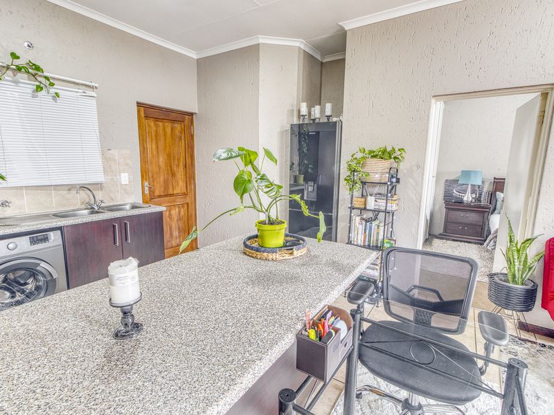 Open-plan kitchen area featuring granite countertops, built-in cabinetry, and an integrated washing machine, with direct access to an adjacent bedroom.