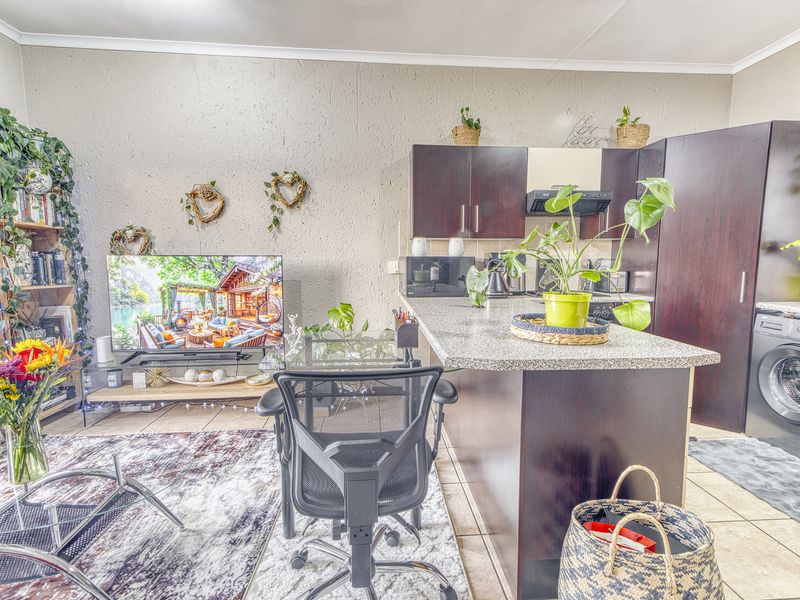 Open-plan living area featuring a compact kitchen with dark wood cabinetry, granite countertops, and an integrated washing machine, seamlessly connecting to the living space.