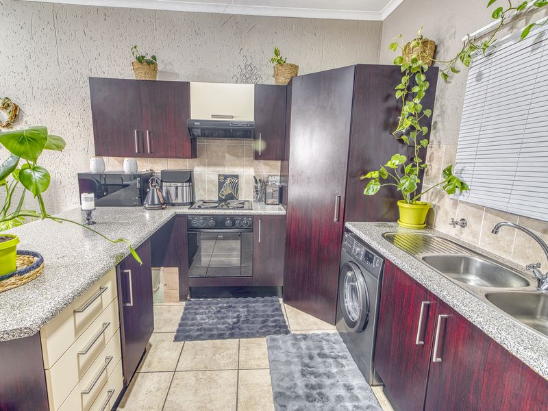 Functional kitchen featuring dark wood cabinetry, granite countertops, built-in oven with hob, extractor fan, and a double bowl stainless steel sink.