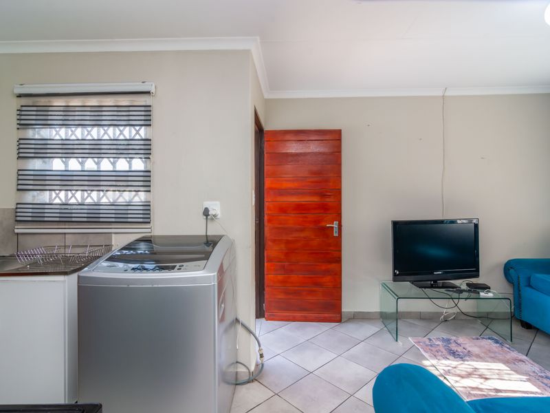 Open plan living area featuring tiled flooring, a compact kitchen corner with sink and cabinetry, and a solid timber door.
