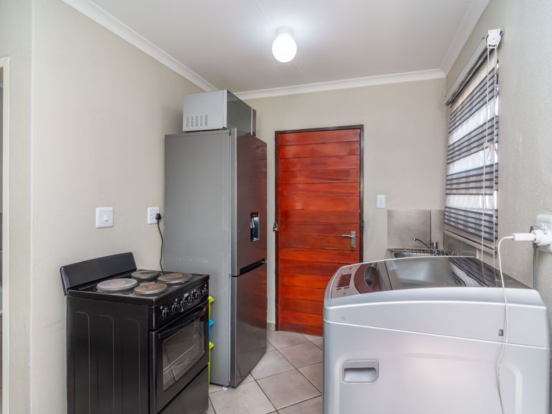 A functional laundry area featuring tiled flooring, a sink, and dedicated plumbing and electrical connections for appliances.