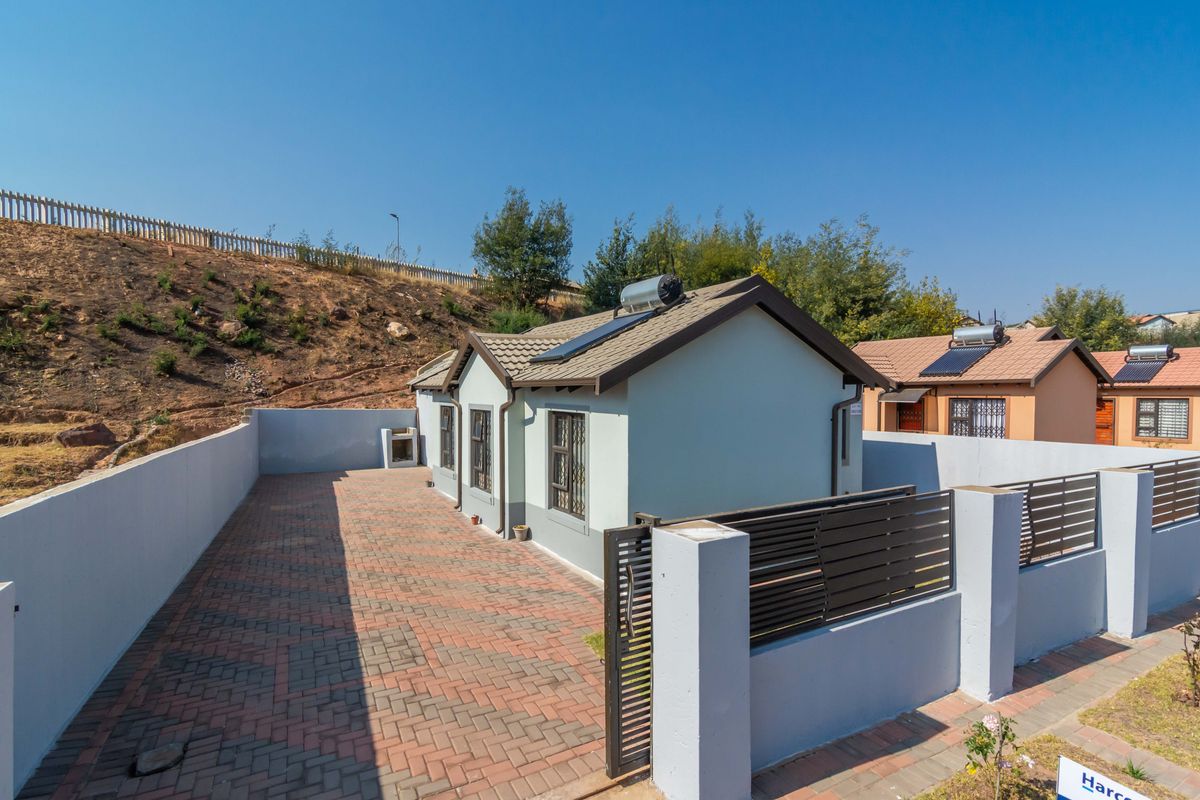 Rear view of the property featuring a paved courtyard, perimeter walling, and a solar water heating system installed on the tiled roof.