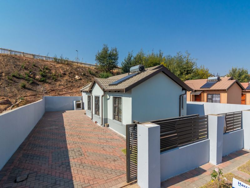 Rear view of the property featuring a paved courtyard, perimeter walling, and a solar water heating system installed on the tiled roof.