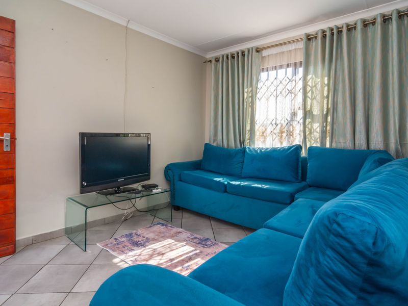 A functional living room featuring tiled flooring, a solid timber door, and a window fitted with a security gate.