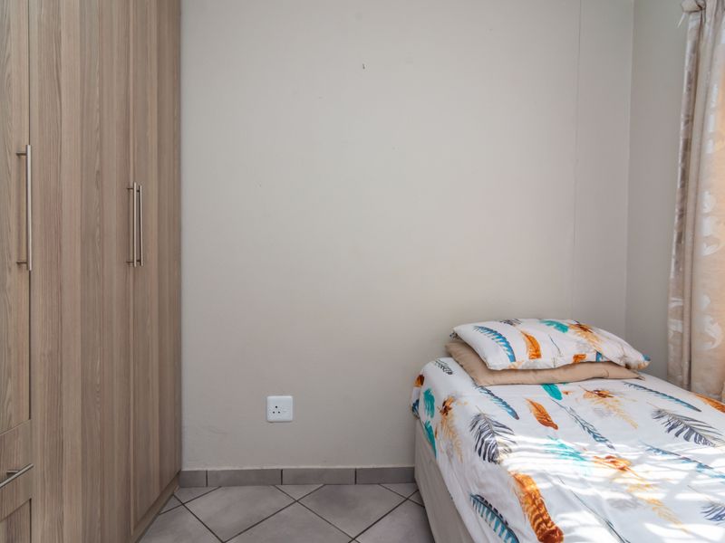 A compact bedroom featuring built-in wooden wardrobes and tiled flooring, providing a functional and neutral living space.