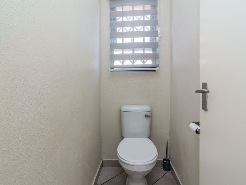 A compact, functional guest toilet featuring tiled flooring and a window with a fitted blind.