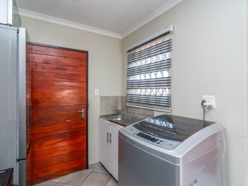 Functional laundry area featuring built-in cabinetry, a stainless steel sink, and tiled flooring with direct access to the exterior.