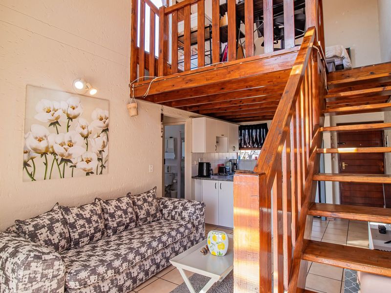 Open-plan living area featuring a timber staircase leading to a mezzanine loft, tiled flooring, and a compact kitchen with built-in cabinetry.