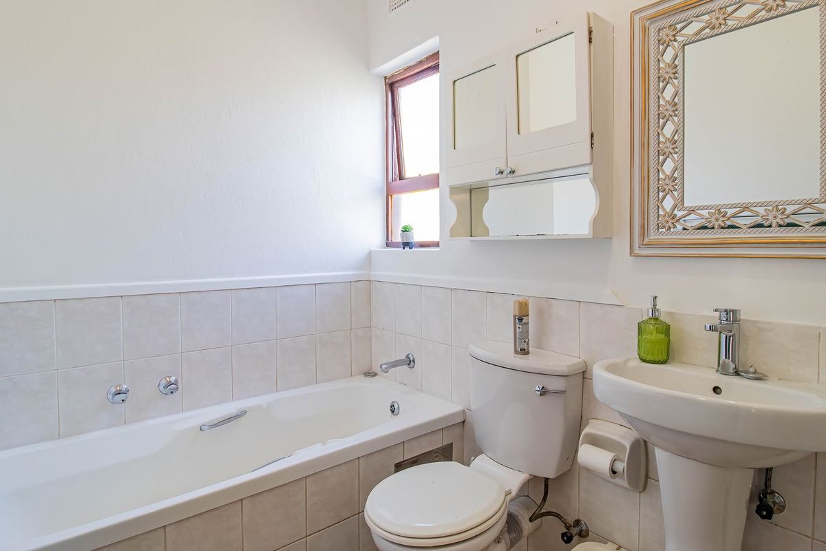 A functional bathroom featuring a bathtub, pedestal basin, and wall-mounted storage cabinet with neutral wall tiling.