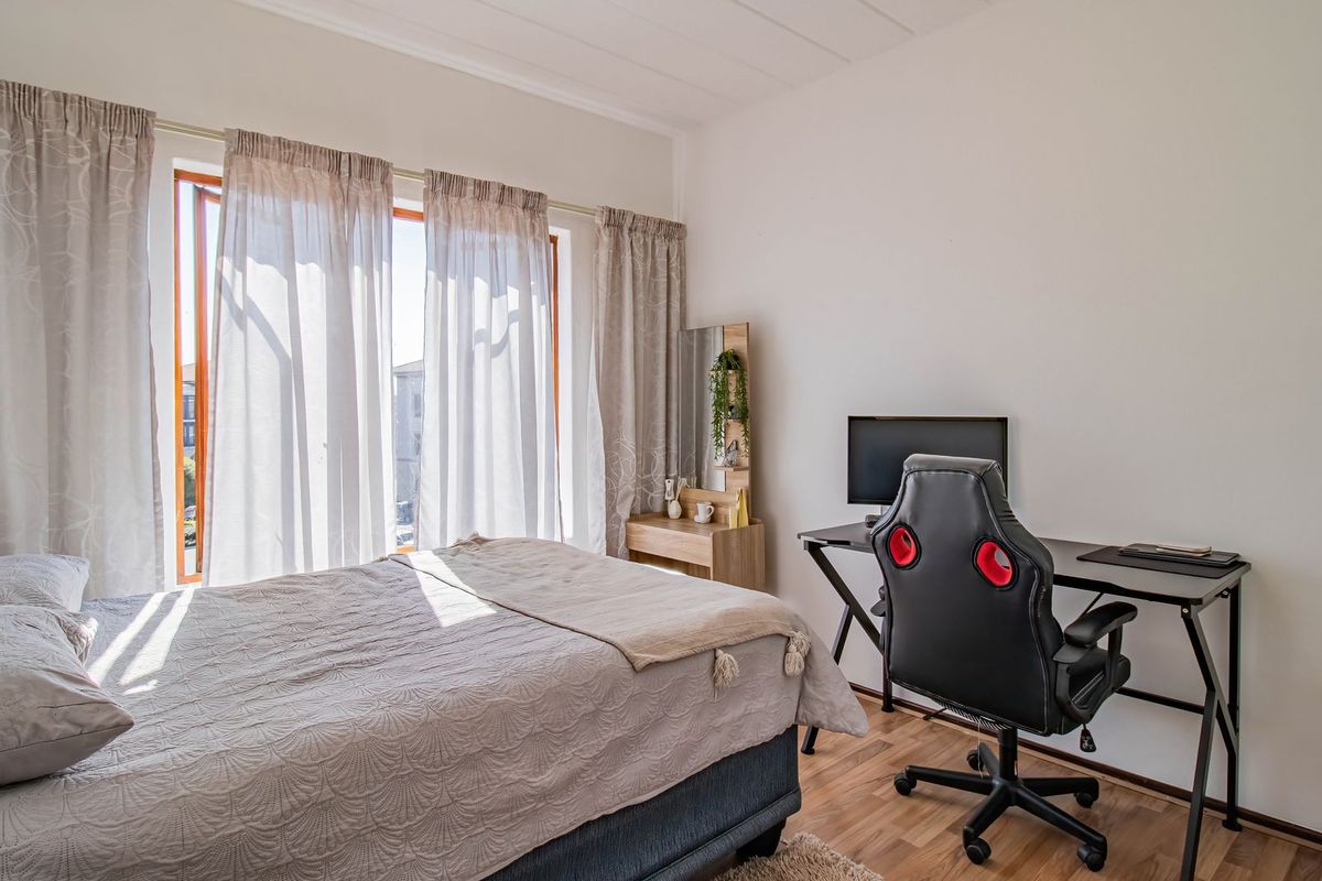 A bright bedroom featuring laminate flooring and a large window with natural light, providing a comfortable and functional living space.