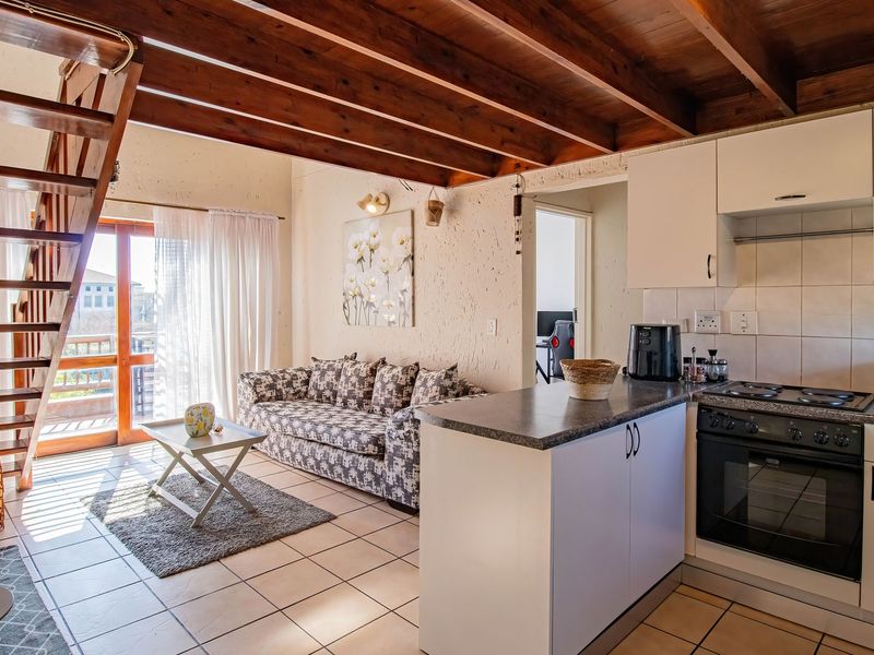 Open-plan living area featuring a kitchen with built-in appliances, tiled flooring, exposed timber ceiling beams, and a timber staircase leading to the upper level.