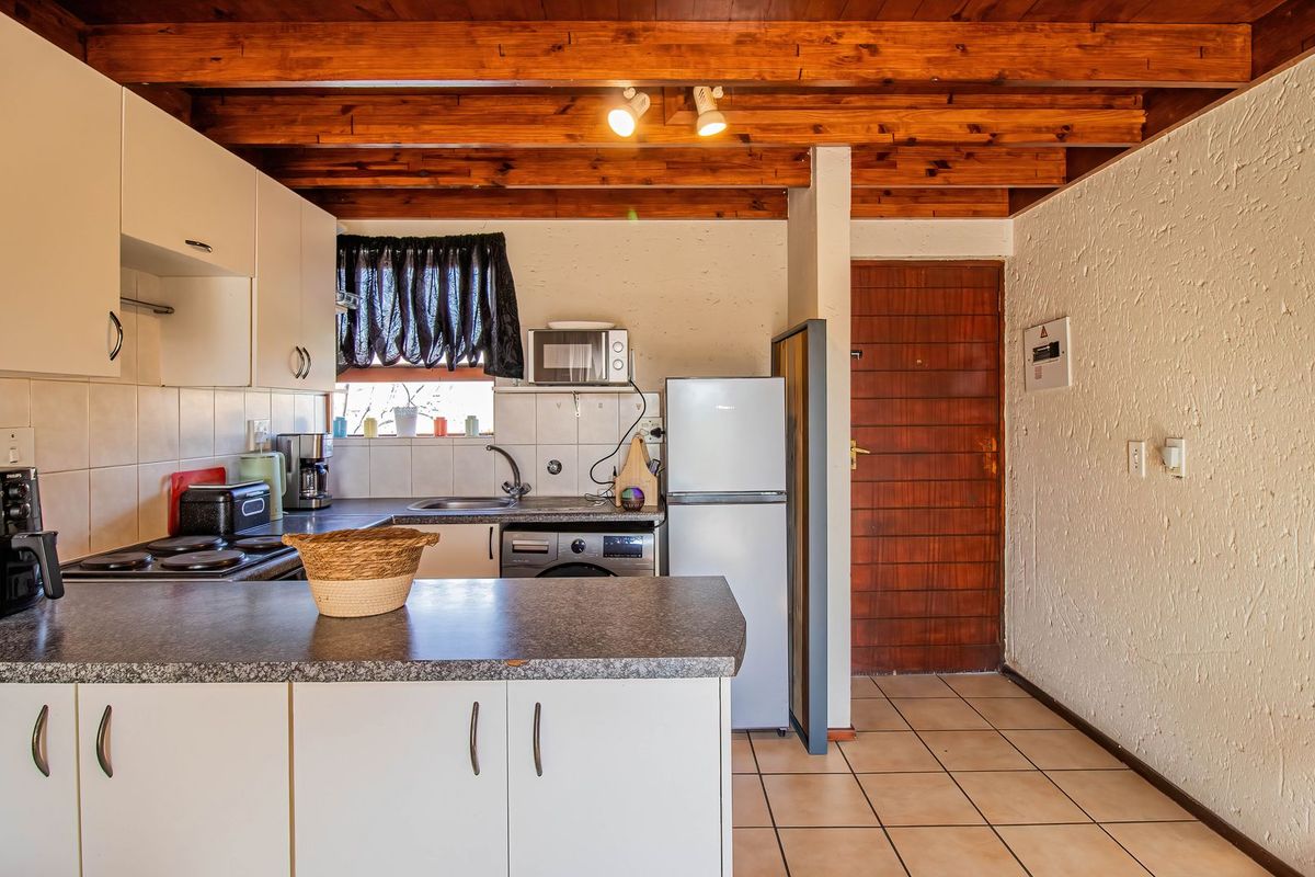 Functional kitchen featuring white cabinetry, laminate countertops, tiled backsplash, and exposed timber ceiling beams, providing a practical layout for daily use.