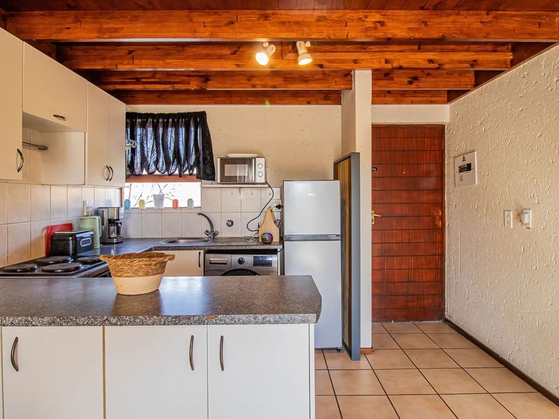 Functional kitchen featuring white cabinetry, laminate countertops, tiled backsplash, and exposed timber ceiling beams, providing a practical layout for daily use.