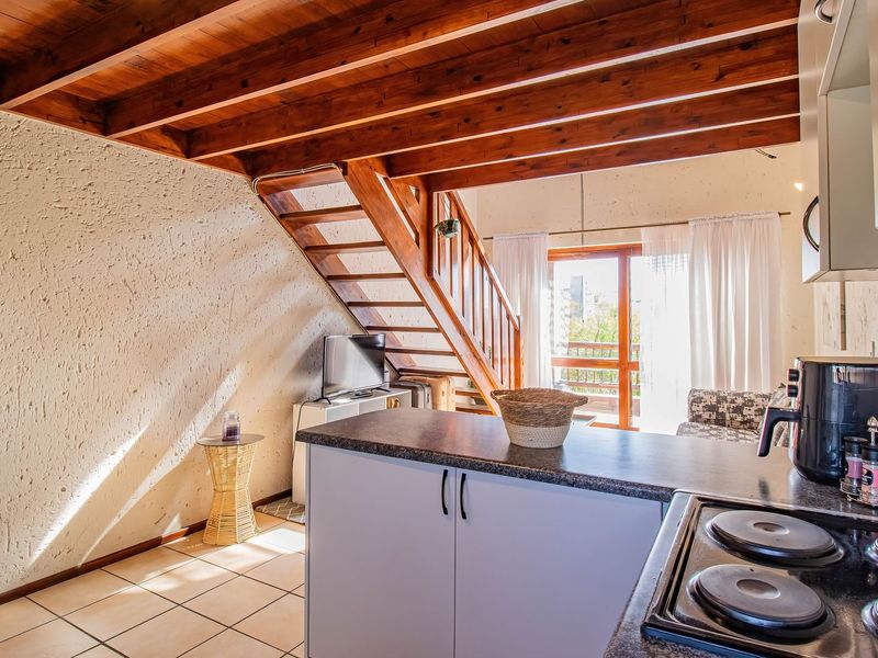 Open-plan kitchen and living area featuring exposed timber ceiling beams, a wooden staircase, and direct access to a balcony through sliding glass doors.