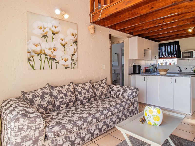 Open-plan living area featuring a compact kitchen with white cabinetry, tiled floors, and exposed timber ceiling beams leading to a mezzanine loft level.