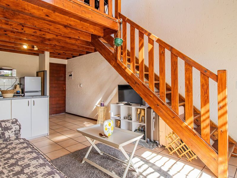 Open plan living area featuring a wooden staircase leading to a mezzanine level, tiled flooring, and a compact kitchen with built-in cabinetry.