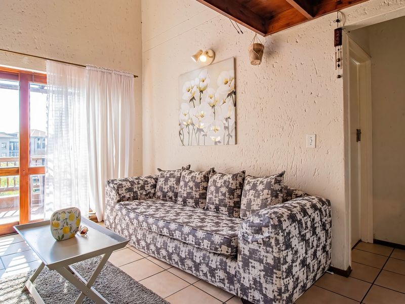 A living room featuring textured walls, tiled flooring, and timber ceiling beams, with a sliding glass door providing access to an outdoor balcony.
