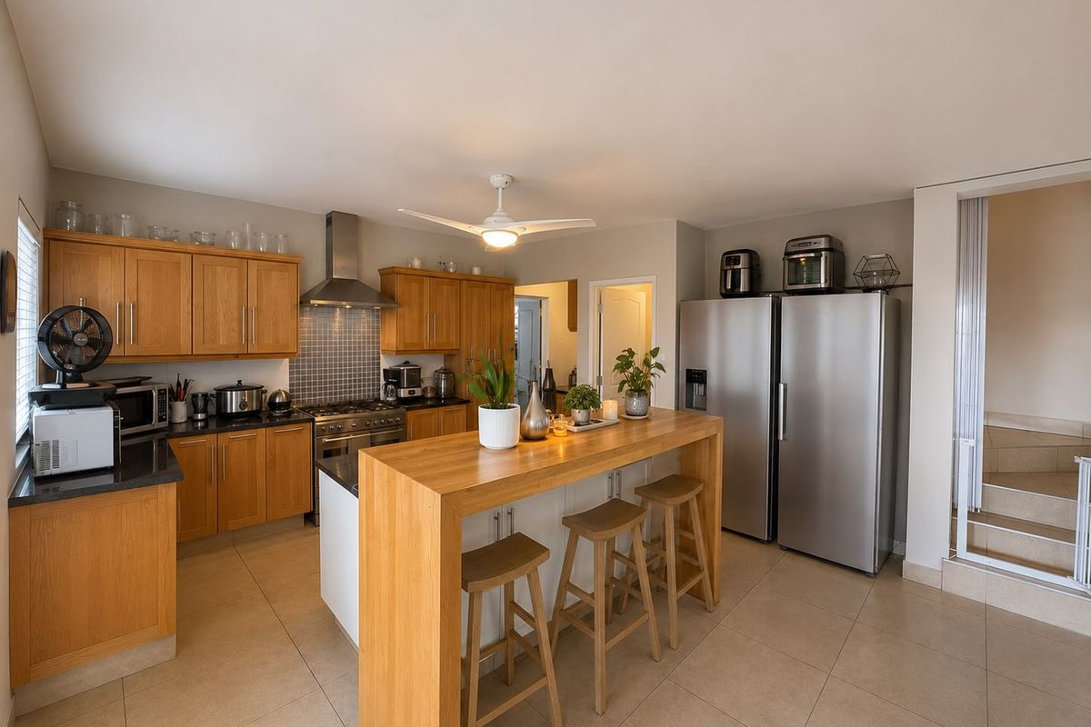 A well-maintained kitchen featuring wooden cabinetry, granite countertops, a gas hob with extractor fan, and a central breakfast bar island.
